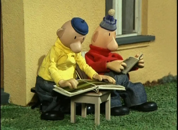 pat and matt (stop-motion characters) reading books while sitting outside, next to a wall.