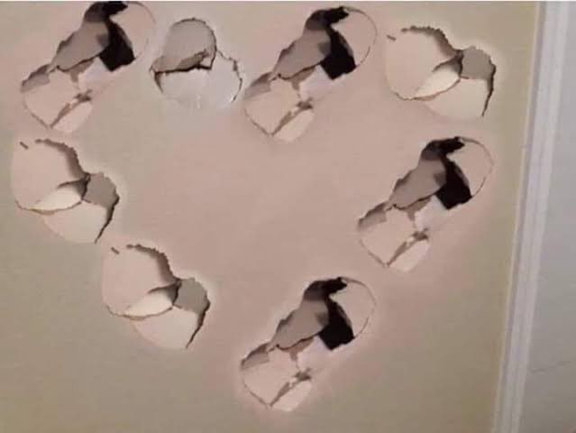 A wall with several punched-in holes. The holes resemble a heart.